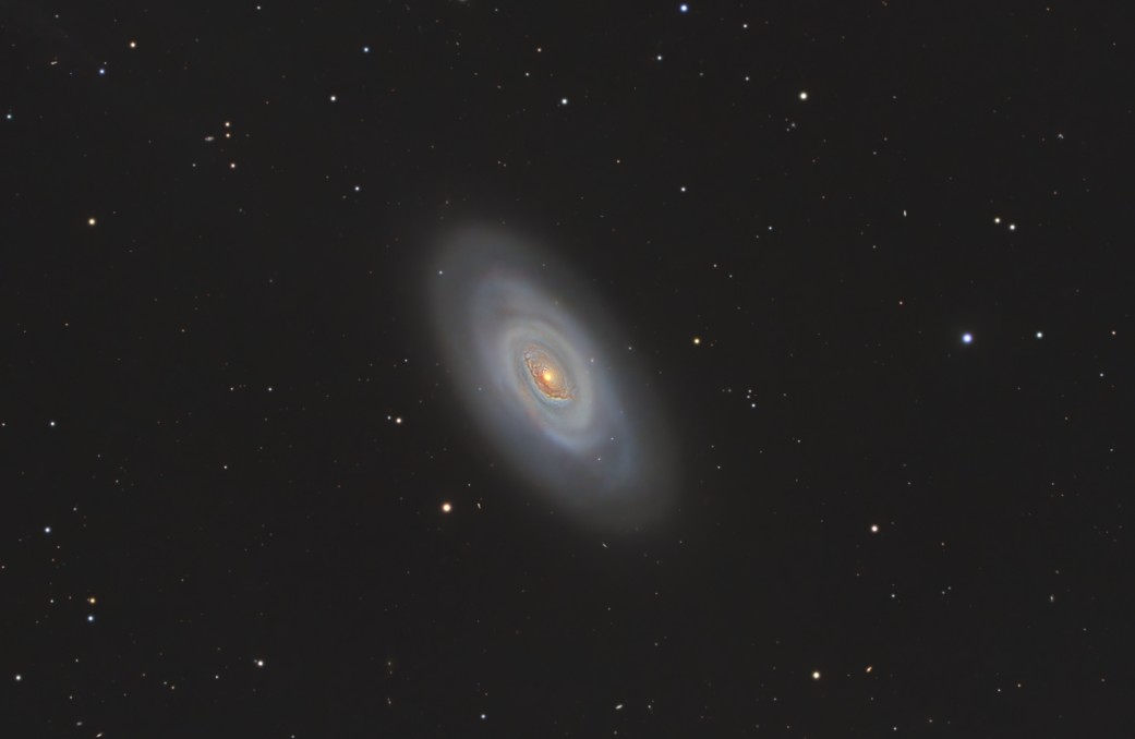 The Black Eye Galaxy (M64), featuring a bright yellowish core partially obscured by a dark, prominent dust lane that gives it its “black eye” appearance, surrounded by spiral arms with star-forming regions, captured in sharp detail by astrophotographer Dr