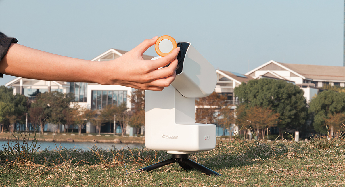 The ZWO Seestar S30 on grass with a person attaching a solar filter