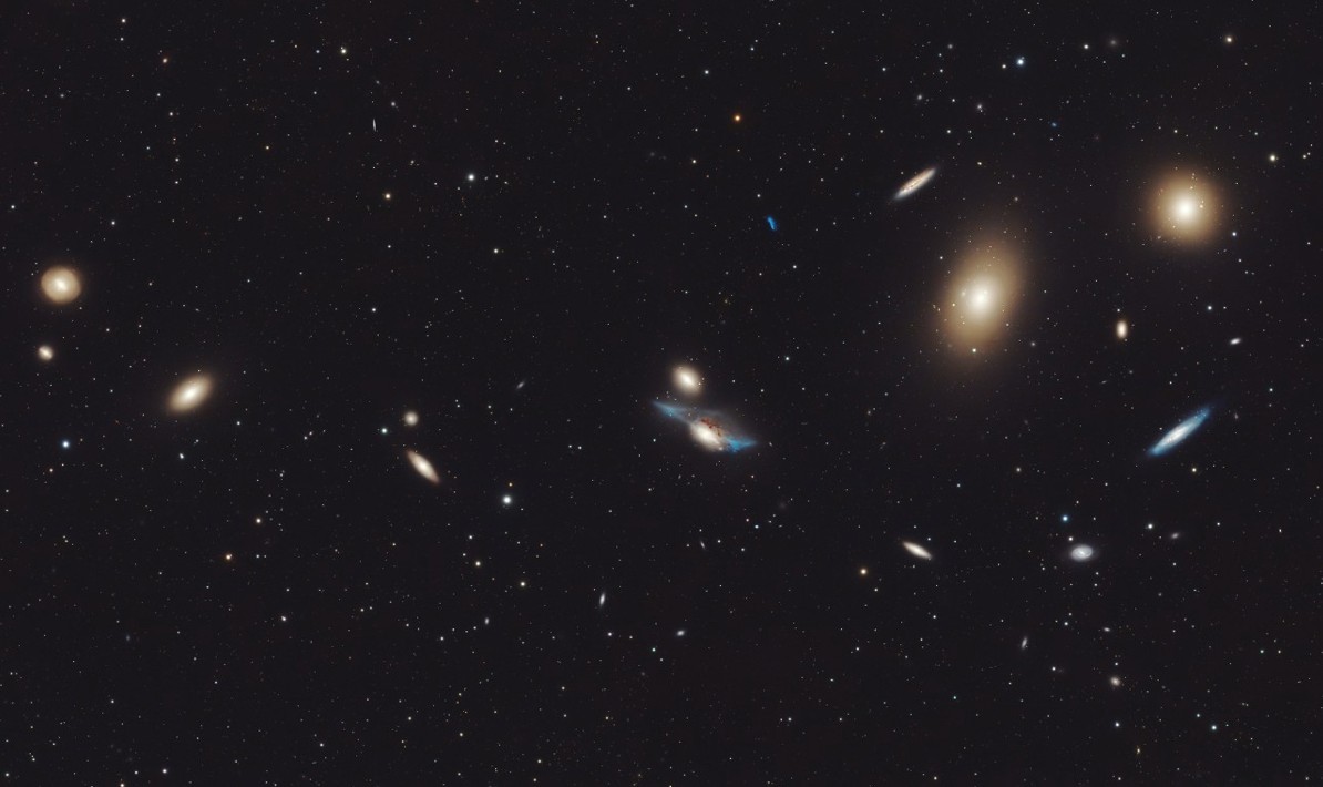 Markarian’s Chain, a striking linear arrangement of several bright galaxies of various shapes and sizes, connected by faint streams of stars and gas, set against a dark starry background.