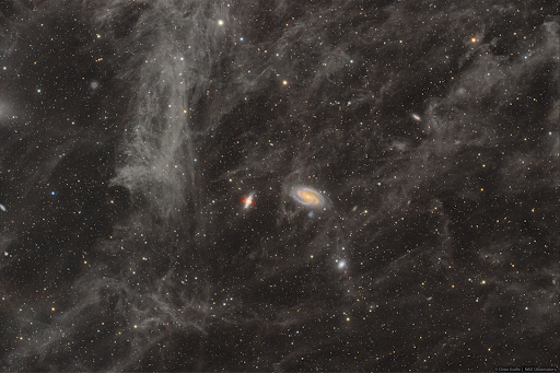 The spiral galaxy M81 with its bright core and well-defined arms, alongside the irregular, starburst galaxy M82 with its elongated shape and red hydrogen outflows, set against a faint backdrop of grey wispy clouds known as Integrated Flux Nebula (IFN).